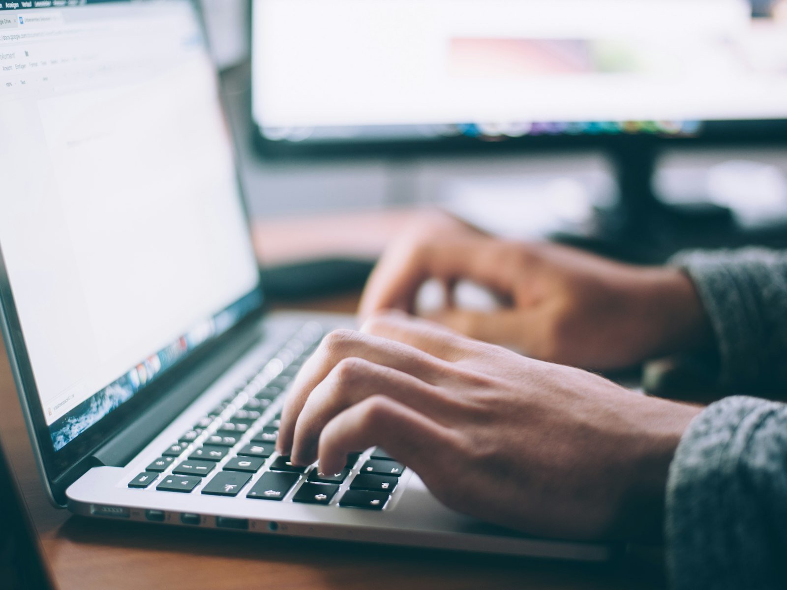 Hands typing on a laptop at a work desk